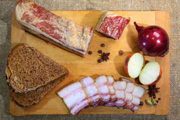Smoked bacon, sliced on a wooden plank. Smoked bacon, red onion, salt and pepper on a clay dish. Smoked lard.