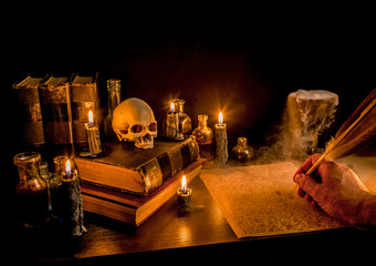 Wizard's Desk. A desk lit by candle light. A human skull, old books, a goblet, and potion bottles also present. A hand writes with a feather quill pen. Thick fog flows from a goblet. Focus on skull.