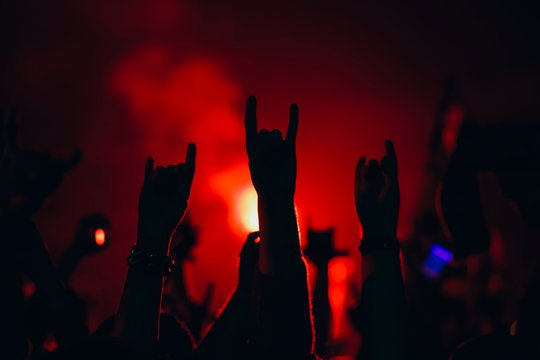 Hands with horns raised up in a colorful lights of night club show with the fire background