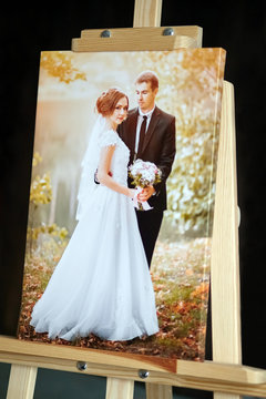 Printing products: Photography with gallery stretch on a frame and standing on a wooden easel. Printed wedding photo on glossy synthetic canvas