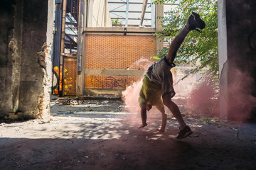 Young man doing parkour handstand around colored smoke bomb