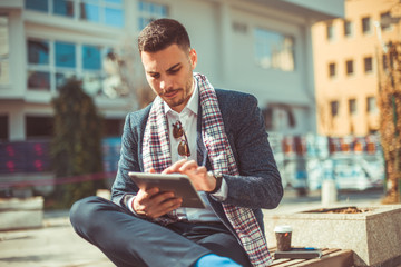 Good looking guy with his coffee and tablet sitting on bench