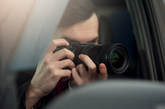 Young Male Spy Sits In The Car Taking Photos To The Camera With A Zoom Lens. Detective Agency Concept
