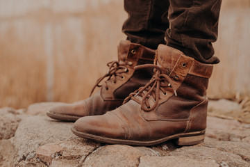 Image of man in brown old leather boots and trousers stands on stones against blurred background. Shabby shoes. Selling of shoes. Coming winter
