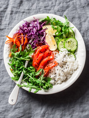 Smoked salmon, rice, vegetables buddha power bowl on gray background, top view. Red cabbage, carrots, arugula, rice, smoked salmon fish bowl. Healthy food concept