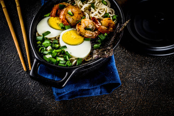 Traditional asian food, ramen soup with shrimp, noodles, spring onion, sliced eggs, mushrooms, on dark concrete background with chopsticks copy space top view