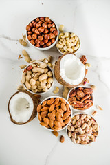 Various types of nuts - walnuts, pecans, peanuts, hazelnuts, coconut, almonds, cashews, in bowls, on a white marble table top view