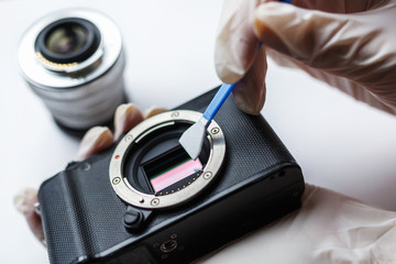 Close-up of mirrorless digital APS-C dirty camera matrix sensor cleaning and maintenance with swab, photographer cleaning photocamera on white background