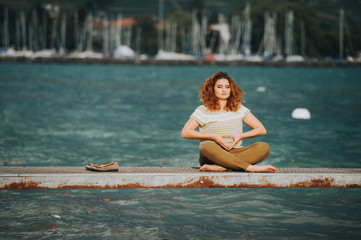 Young beautiful woman in lotus position meditating on the lake side on a srormy day
