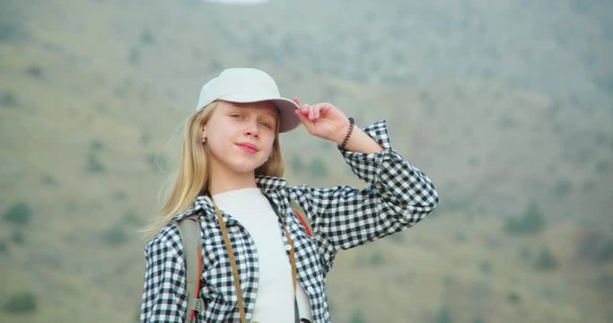 The girl waves her blond hair in the mountains and puts a cap on her head. 4K slow motion video