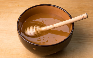 Honey dipper lying in bowl close-up. Healthy natural sweet syrup.