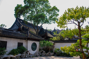 Fototapeta na wymiar Chinese walled garden in Shanghai China. Stone walls, tiled roofs, trees and large rocks.