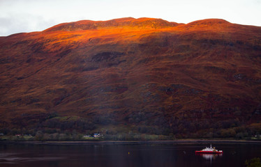 View of the mountains at the fiord Loch Linnhe, Scotland, at early morning in a warm red light with a ship 