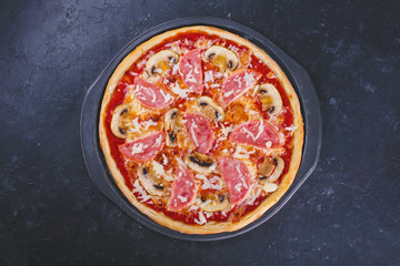pizza with bacon ,cheese and tomatoes on a darkbackground