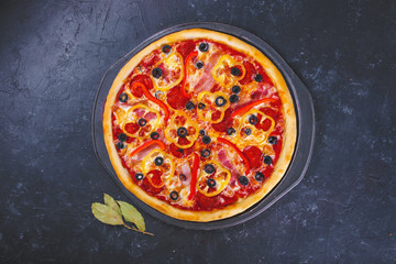 Pizza with cheese meat peppers and tomatoes on a dark background