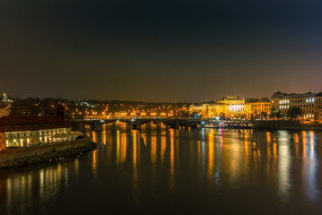 Fototapeta na wymiar Illuminated classical buildings and street lights reflecting on the Vltava river in Prague in a cold winter night - 1