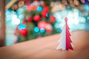 Plastic red and white Christmas tree decoration on the wood table with blur big Christmas tree behide.
