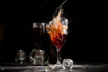 The breaking of a glass with fragments. The explosion of a glass on a black background with a colored liquid. Splashes of colors.