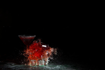 The breaking of a glass with fragments. The explosion of a glass on a black background with a colored liquid. Splashes of colors.