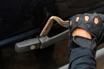 Bandit in black gloves breaking in car lock with crowbar tool.Car jacking concept