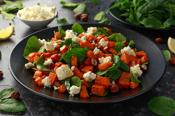Healthy roasted sweet potato salad with spinach, feta cheese, hazelnut nuts in black plate
