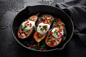 Grilled eggplants with yogurt sauce, pomegranate seeds, parsley and green onion in cast iron vintage pan.
