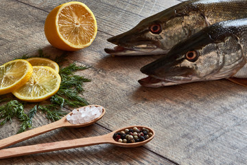 Two fresh pike fish on a wooden table with spices, dill, Himalayan salt and lemon. Close up top view