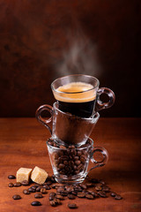 glass cups, in sequence vertically, with coffee beans, ground, and steaming drink. still life