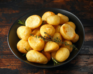 Roast golden potatoes seasoned with salt, garlic, rosemary and thyme on rustic wooden background