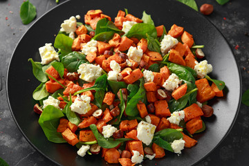 Healthy roasted sweet potato salad with spinach, feta cheese, hazelnut nuts in black plate
