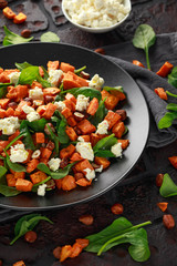 Healthy roasted sweet potato salad with spinach, feta cheese, hazelnut nuts in black plate, rustic background