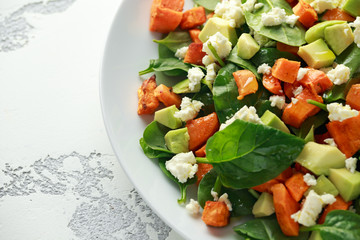 Avocado, roasted sweet potato, spinach, feta cheese healthy salad in white plate.
