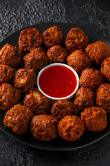 Indian Pakora snack spicy onion, red pepper with chilli sauce in a black plate