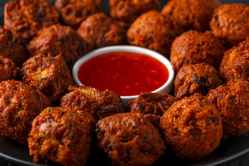 Indian Pakora snack spicy onion, red pepper with chilli sauce in a black plate