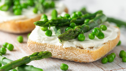 Appetizer bruschetta, toast with Asparagus, Peas and creamy soft cheese on white board. healthy food.