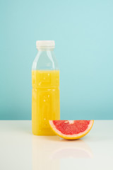 Orange drink and slice of grapefruit on white and blue background. Minimalistic image of citrus juice bottle and fruit at sparse bright environment.