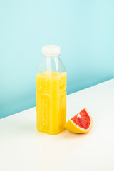 Orange drink and slice of grapefruit on white and blue background. Minimalistic image of citrus juice bottle and fruit at sparse bright environment.