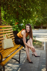 glamorous business girl with a bag sits, straightens the shoes on her foot on a park bench.