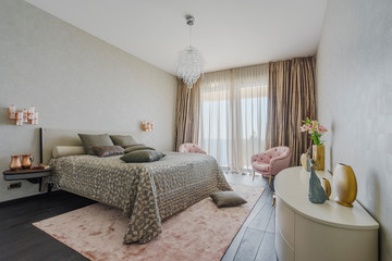 Interior of a spacious light bedroom with windows in a luxury villa. Big comfortable double bed in elegant modern bedroom