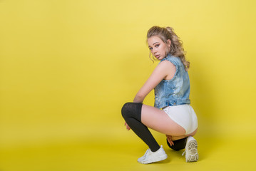 Fototapeta na wymiar Attractive girl dancer sportswoman in shorts sitting on the floor color background, twerk