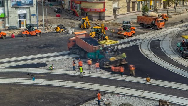 Asphalt paver, roller and truck on the road repair site during asphalting timelapse. Road construction equipment.