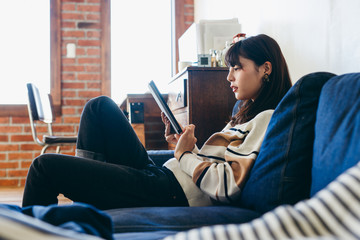Woman sitting on sofa and using digital tablet