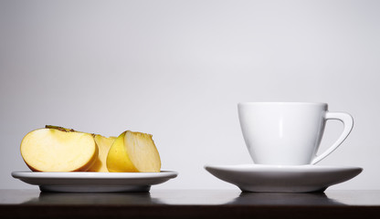 White coffee cup and plate with apples on gray background
