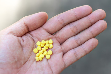 Yellow pills in hand on background.