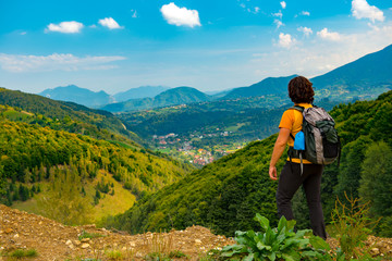 Young mountain hiker enjoying a beautiful mountain landscape covered with lush forests. Hiking in a sunny summer day.