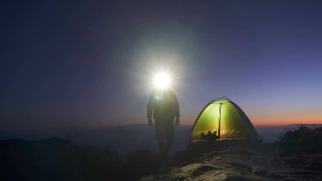 an adult man in an adventure trip to the top of a mountain set up a tourist tent for an overnight stay