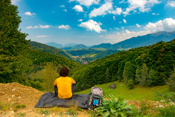 Fototapeta na wymiar Young mountain hiker sitting on a waterproof nylon blanket in a beautiful mountain landscape and enjoying the view. Hiker concept for summer designs.