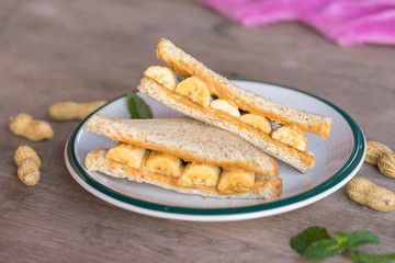 Sandwich whole wheat  with peanut butter and banana on plate.