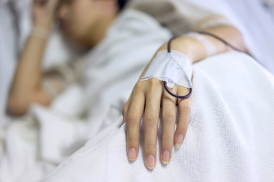 Close up, woman add blood in hand and blurry of patient illness sleeping on hospital bed. Medical equipment concept.