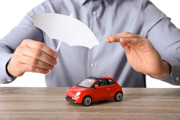 Male insurance agent covering toy car with paper cutout umbrella and hand at table, closeup